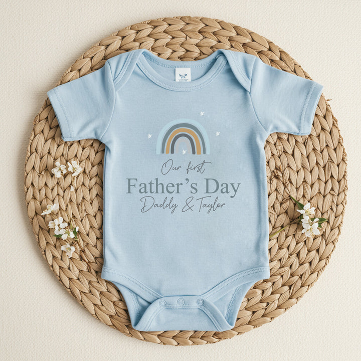 Personalised blue Father's Day baby vestthat says 'Our First Father's Day Daddy & Taylor'. This design features a blue rainbow 