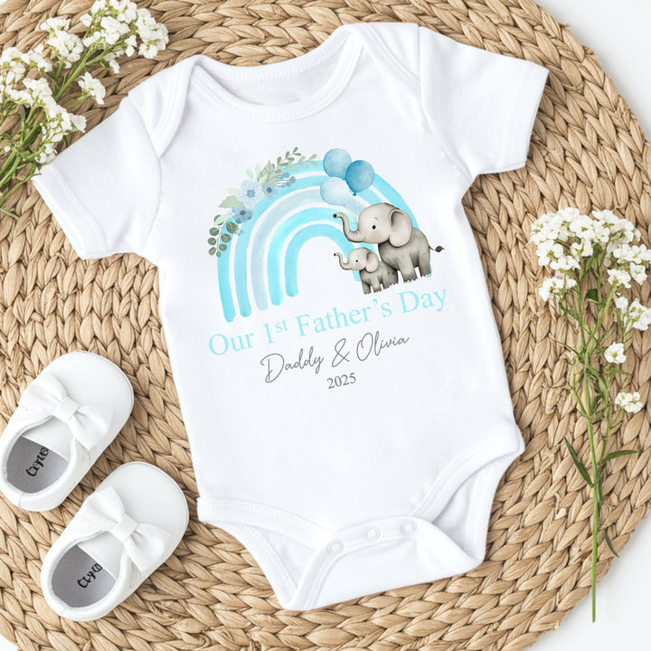 Personalised white Father's Day baby vest that says 'Our 1st Father's Day Daddy & Olivia 2025'. This design features a blue rainbow with 2 grey elephants holding 3 balloons