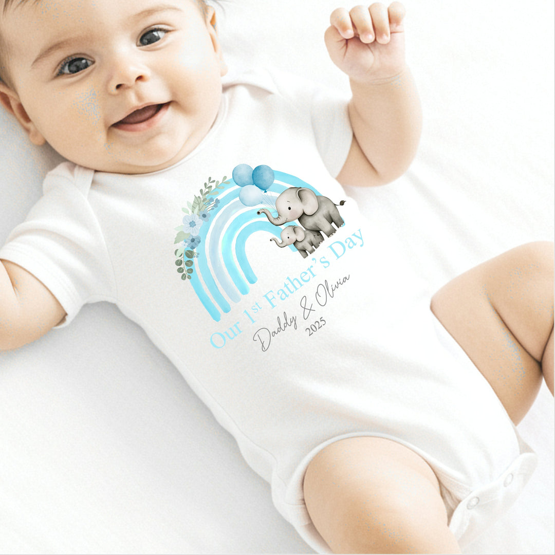 Personalised white Father's Day baby vest that says 'Our 1st Father's Day Daddy & Olivia 2025'. This design features a blue rainbow with 2 grey elephants holding 3 balloons