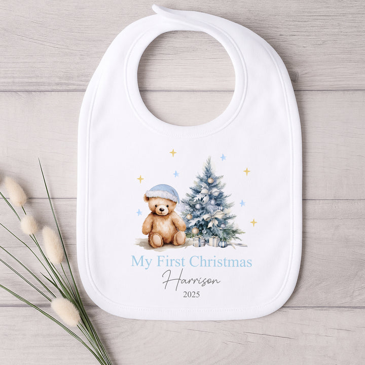 Baby bib with Christmas design featuring a teddy bear and tree, on a wooden surface.