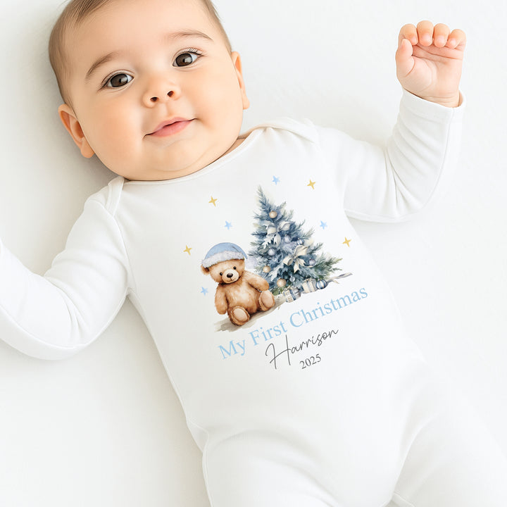 Baby wearing a white onesie with a Christmas design and text, sitting on a white surface.