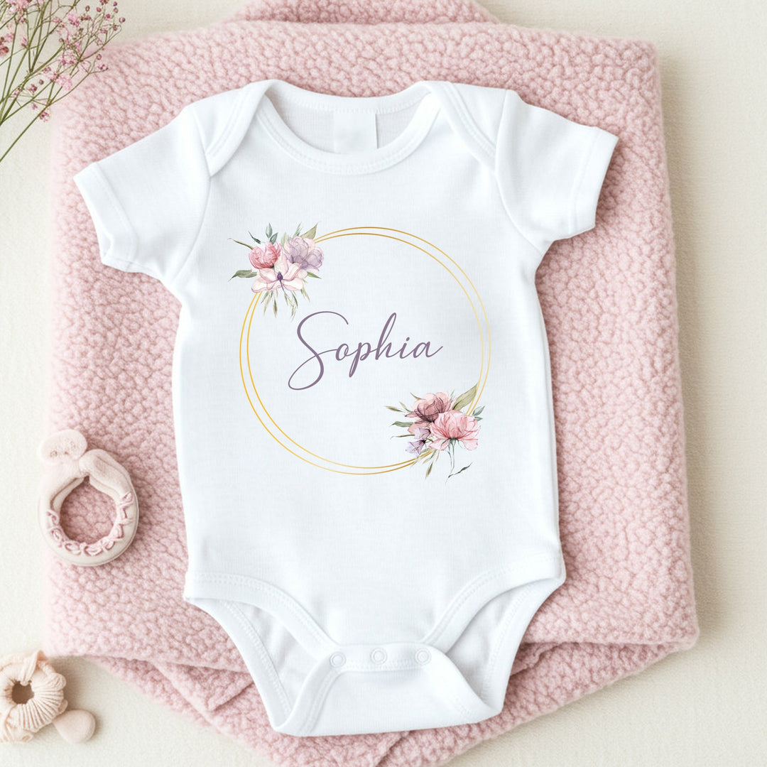 a personalised white baby vest that says 'Sophia'. This design features a purple and pink wreath with a name in the middle of it 