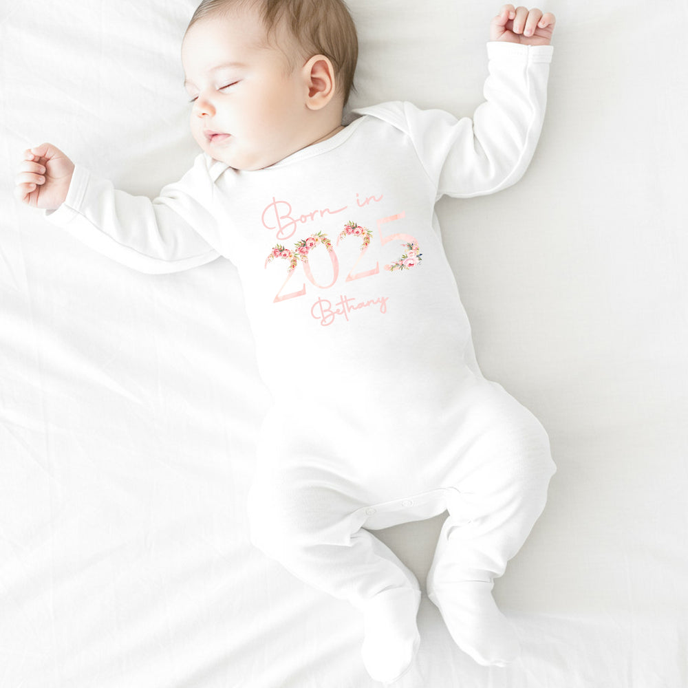 a personalised white baby grow that says 'Born in 2025 Bethany'. This design features a pink floral elements around the 2025