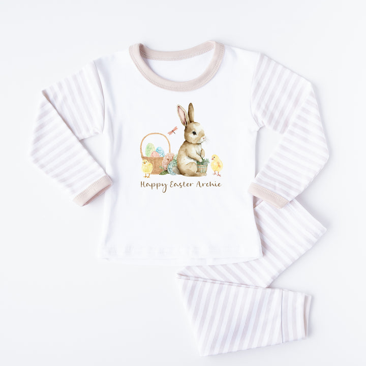 Personalised beige striped Easter Pyjamas that say 'Happy Easter Archie'.  This design features a brown bunny and an easter basket