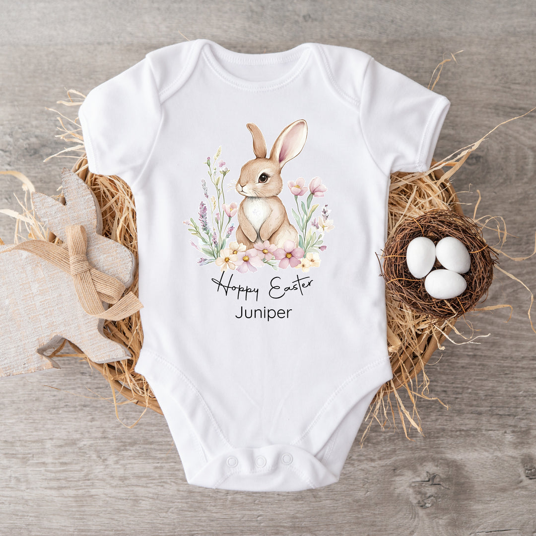 Personalised white Easter baby vest that says 'Hoppy Easter Juniper'. This design features a brown bunny in a floral wreath