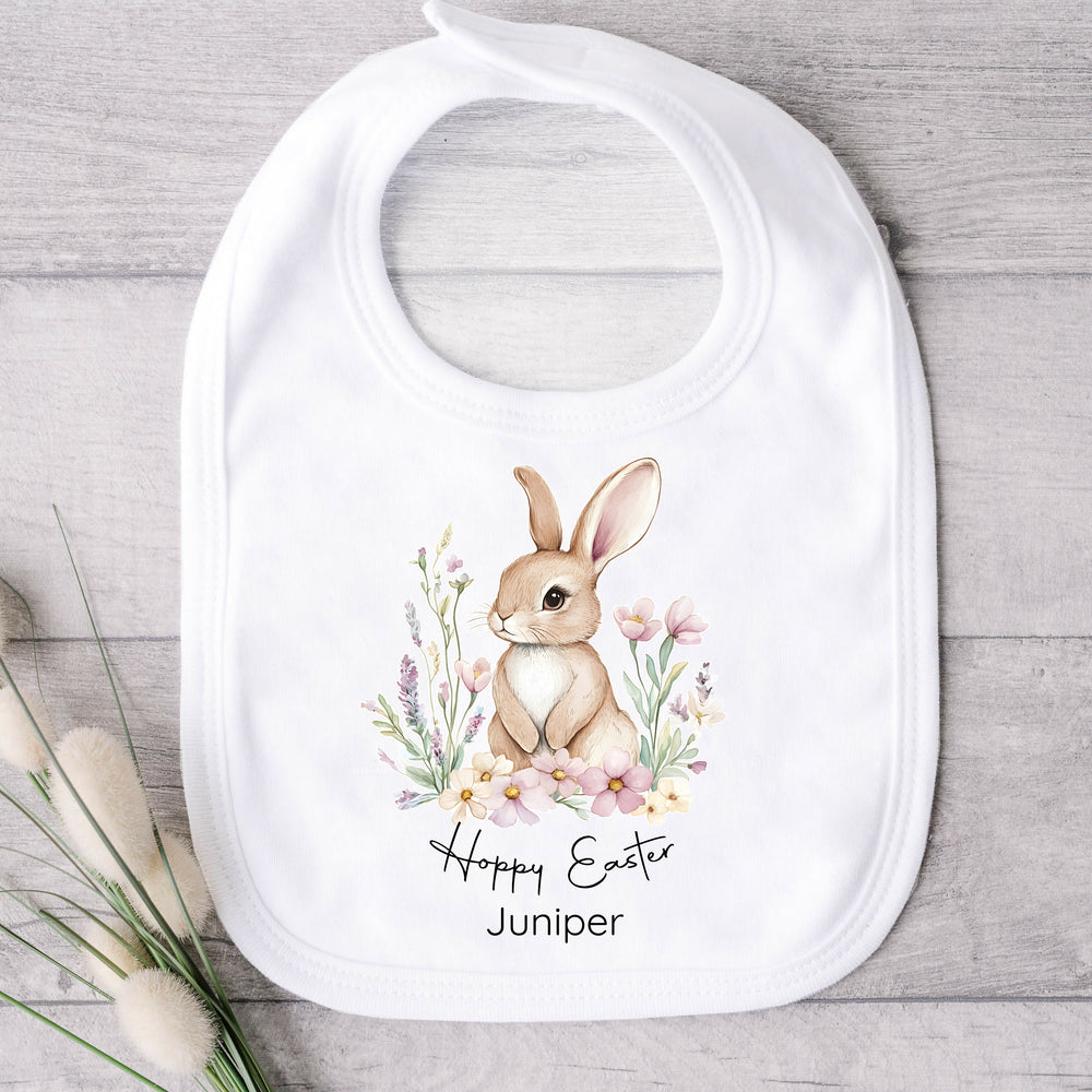 Personalised white Easter baby bib that says 'Hoppy Easter Juniper'. This design features a brown bunny in a floral wreath