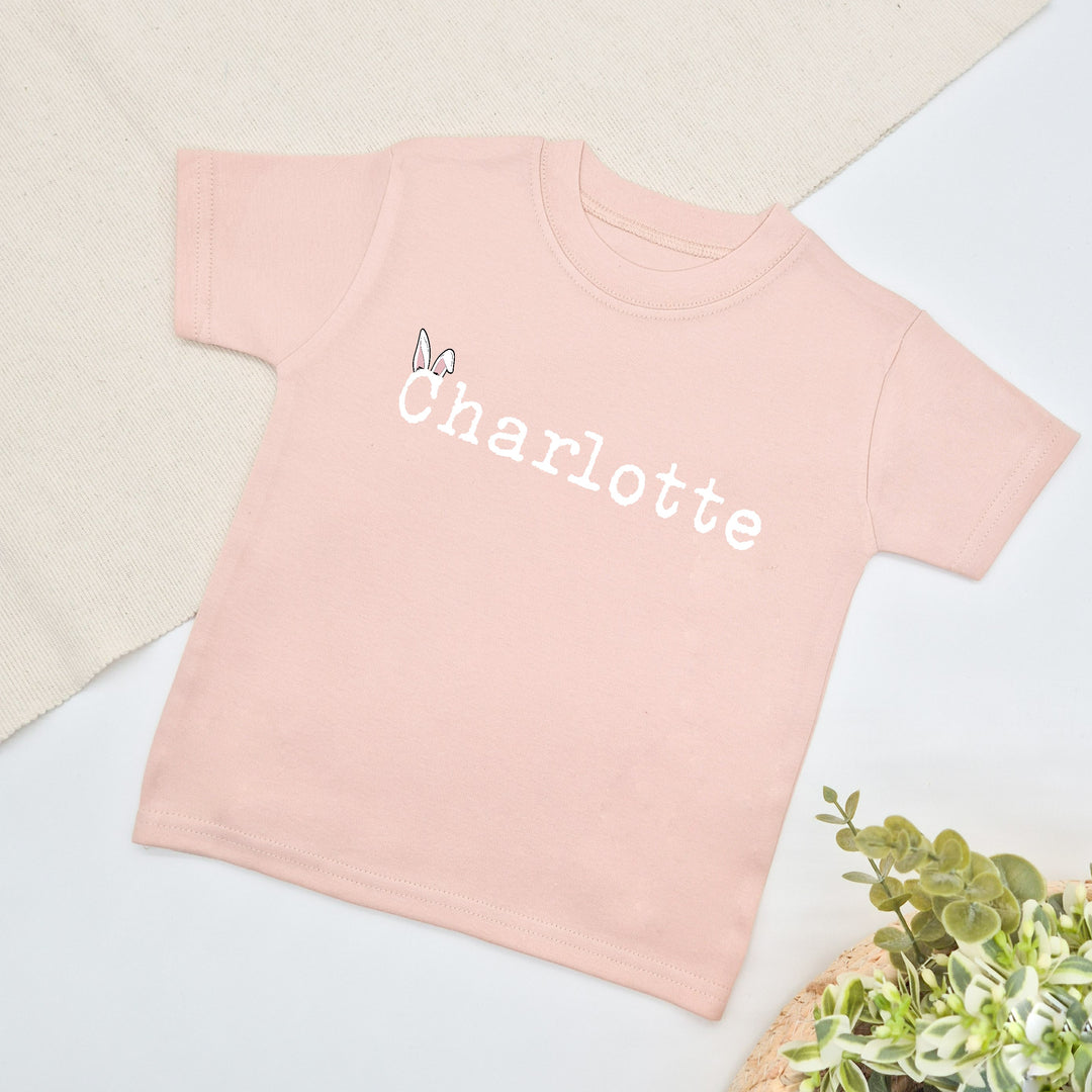 Personalised baby pink Easter childrens t-shirt that says 'Charlotte'. This design features a name with bunny ears on the first letter