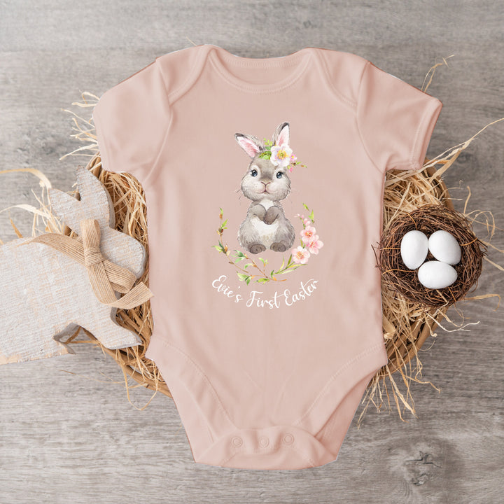 Personalised pink Easter baby vest that says 'Evie's First Easter'. This design features a bunny in a pink floral wreath