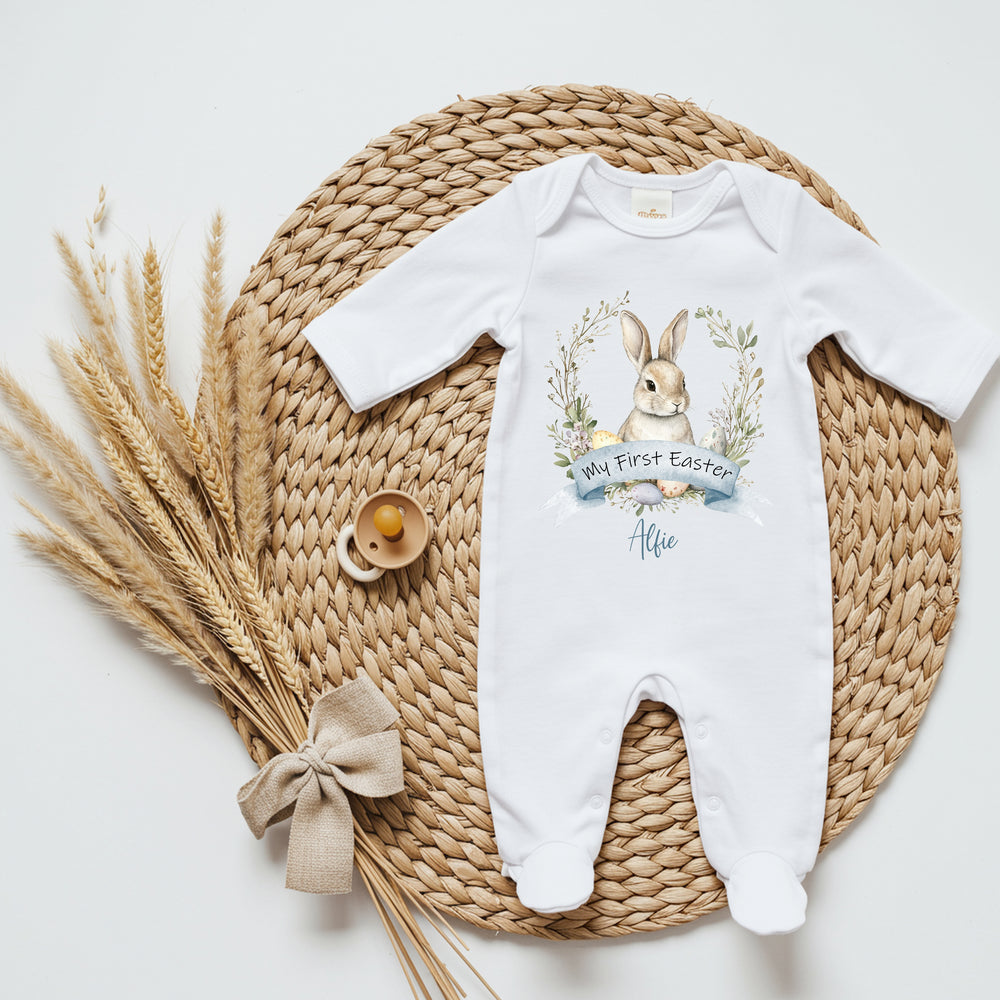 Personalised white Easter baby grow that says 'My First Easter Alfie'. This design features a brown bunny in a wreath with Easter eggs