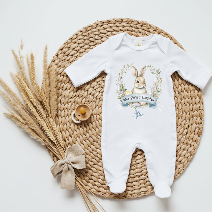 Personalised white Easter baby grow that says 'My First Easter Alfie'. This design features a brown bunny in a wreath with Easter eggs