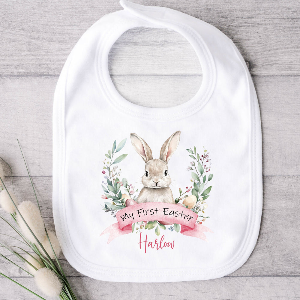 Personalised white Easter baby bib that says 'My First Easter Harlow'. This design features a white bunny in the middle of a wreath with Easter eggs at the bottom of the wreath