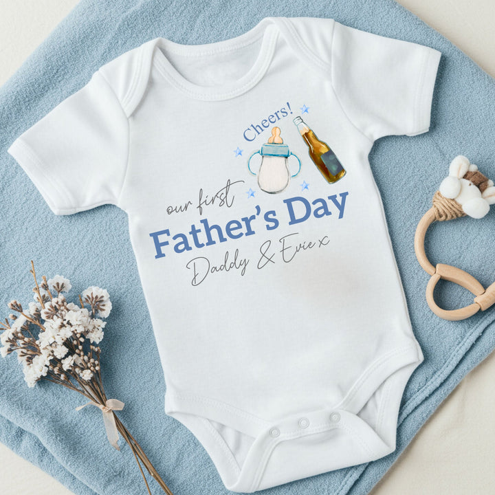 Personalised white Father's Day baby vest that says 'Our First Father's Day Daddy & Evie x'. This design features a milk bottle and beer bottle saying 'Cheers' above it 