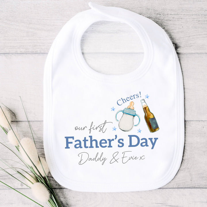 Personalised white Father's Day baby bib that says 'Our First Father's Day Daddy & Evie x'. This design features a milk bottle and beer bottle saying 'Cheers' above it 