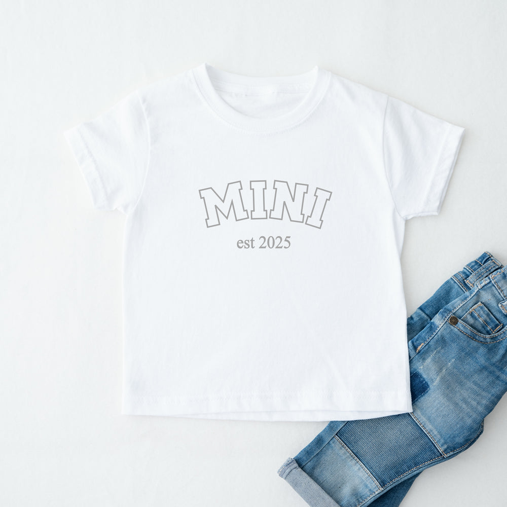 White t-shirt with 'MINI est 2025' text and blue jeans on a white background