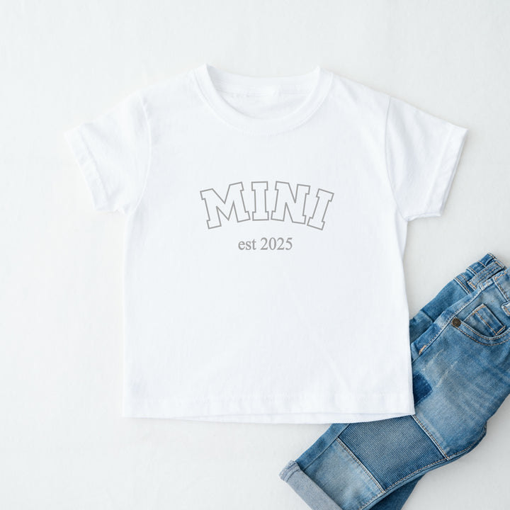 White t-shirt with 'MINI est 2025' text and blue jeans on a white background