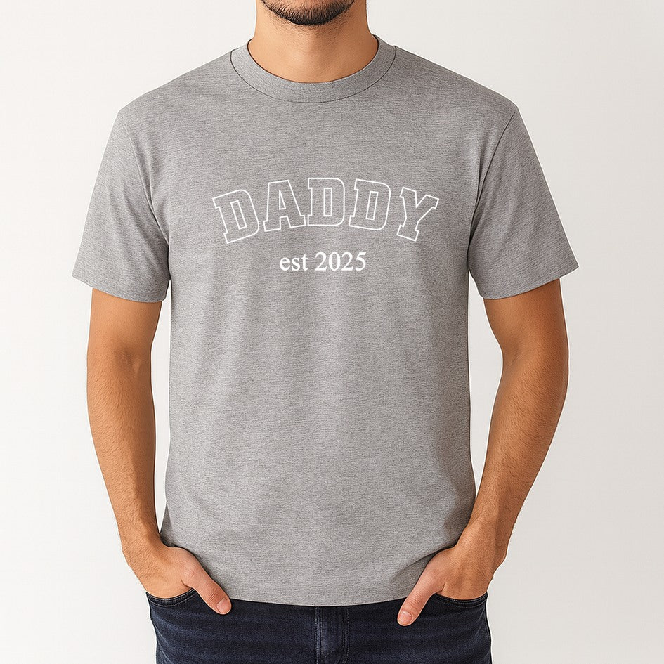 Gray t-shirt with 'DADDY est 2025' text worn by a person on a white background