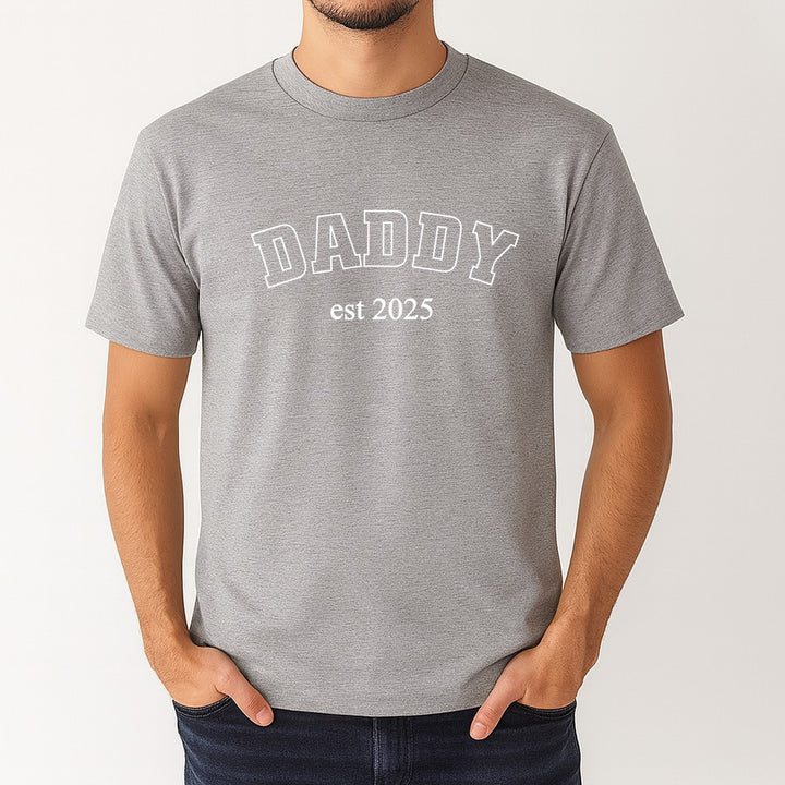 Gray t-shirt with 'DADDY est 2025' text worn by a person on a white background