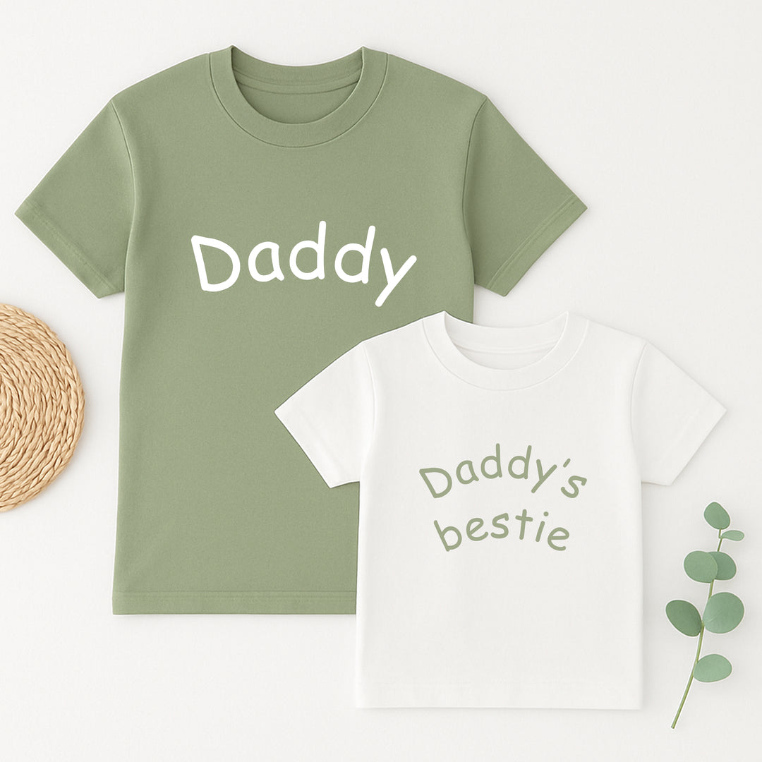 Two children's t-shirts, one green with 'Daddy' and one white with 'Daddy's bestie', on a light background.