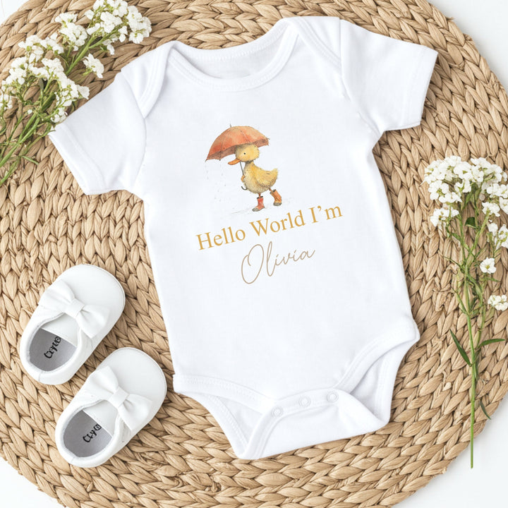 A personalised white baby vest that says 'Hello World I'm Olivia'. This design features a yellow duck holding an orange umbrella