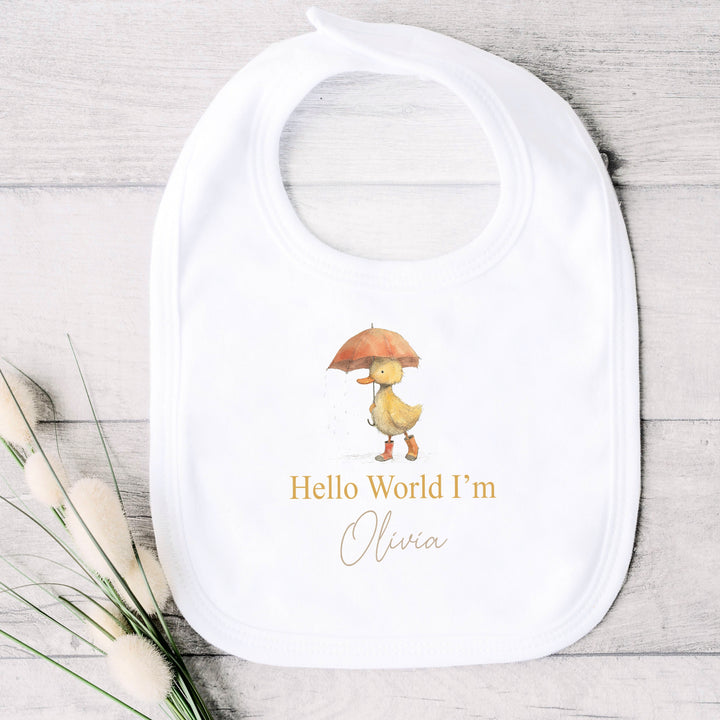 A personalised white baby bib that says 'Hello World I'm Olivia'. This design features a yellow duck holding an orange umbrella