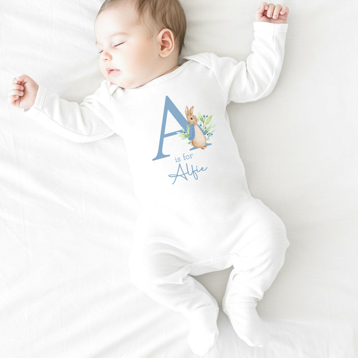 a personalised white baby grow that says 'A is for Alfie' in dusky blue text. This design features a rabbit wearing a dusky blue jacket