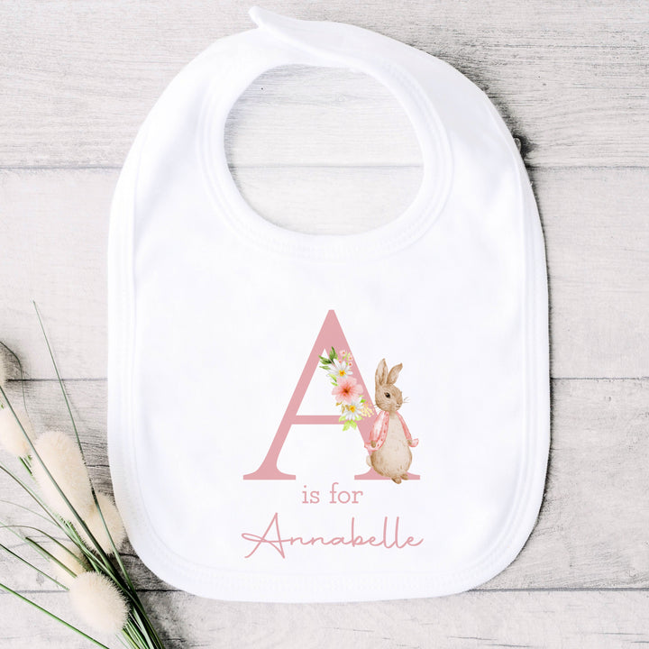 A personalised white baby bib that says 'A is for Annabelle' in pink. This design features a rabbit wearing a pink jacket