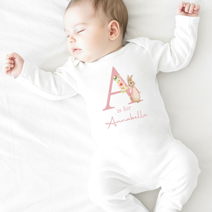 A personalised white baby grow that says 'A is for Annabelle' in pink. This design features a rabbit wearing a pink jacket