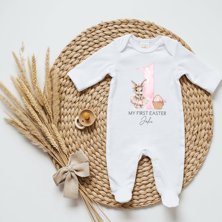 Personalised white Easter baby grow/sleepsuit that says 'My First Easter Jodie'. This design features a big pink 1 with a ballerina bunny one side and an Easter basket with pink Easter eggs in it the other side