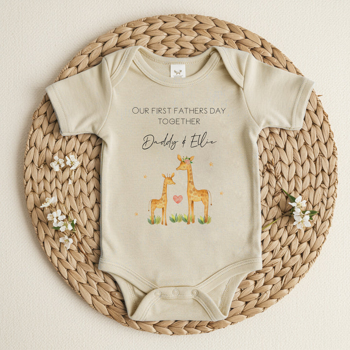 Personalised beige Father's Day baby vest that says 'Our First Father's Day Together Daddy & Ellie'. This design features 2 giraffes