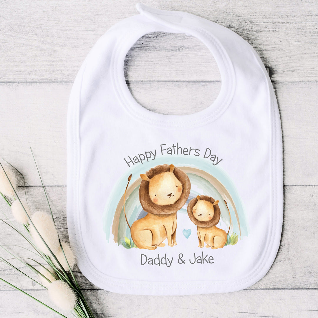 Personalised white Father's Day baby bib that says 'Happy Fathers  Day Daddy & Jake'. This design features a blue rainbow and 2 lions 