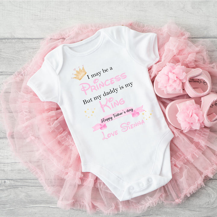 Personalised white Father's Day baby vest that says ' I may be a Princess But my Daddy is my King Happy Father's Day Love Sienna'. This design features a crown and a fairy wand