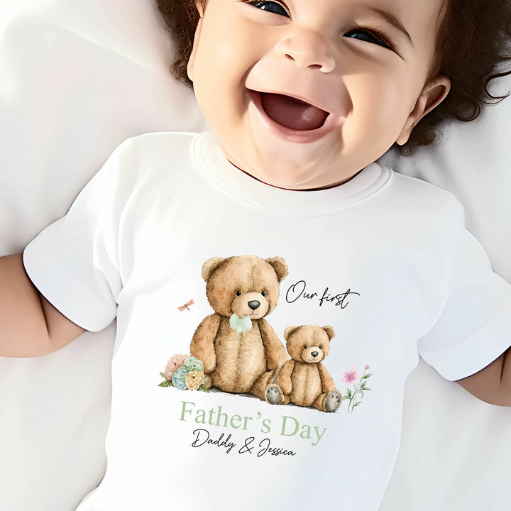 Personalised white Father's Day baby vest that says 'Our first Father's Day Daddy & Jessica'. This design features a big teddy bear wearing a sage green bow tie sitting next to a little teddy bear