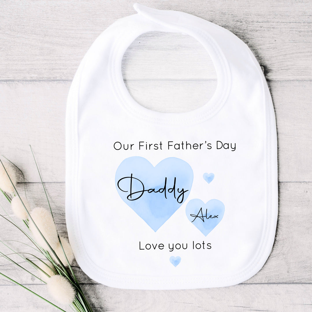 Personalised white Father's Day baby bib that says 'Our First Father's Day Daddy Alex Love you lots'. This design features 2 blue hearts