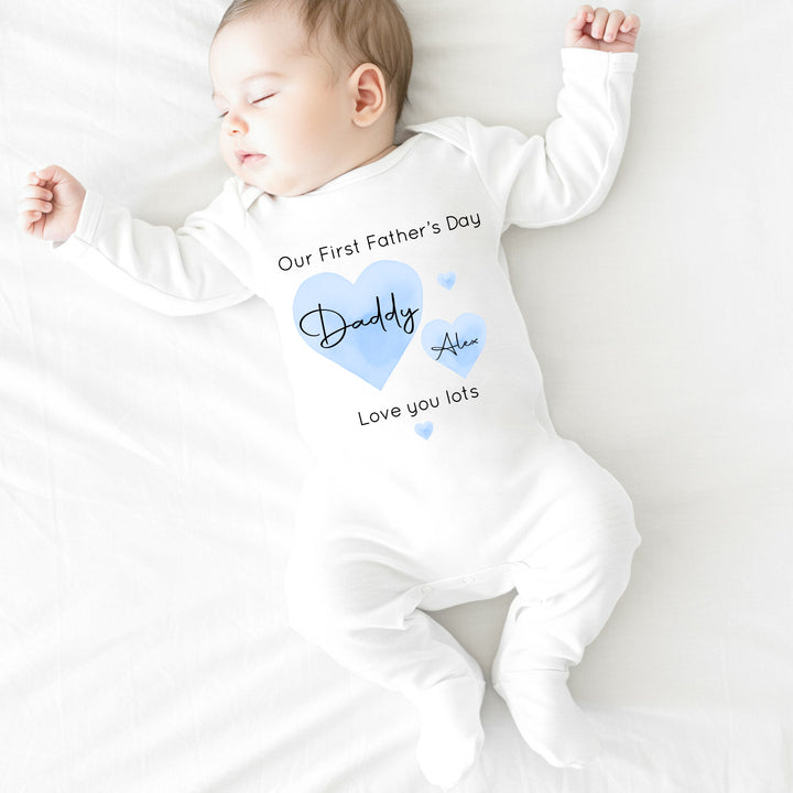 Personalised white Father's Day baby grow/sleepsuit that says 'Our First Father's Day Daddy Alex Love you lots'. This design features 2 blue hearts