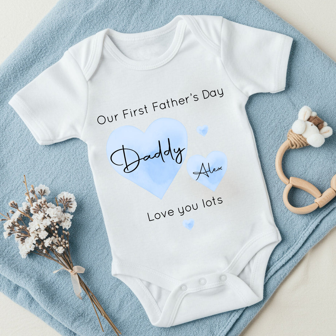 Personalised white Father's Day baby vest that says 'Our First Father's Day Daddy Alex Love you lots'. This design features 2 blue hearts