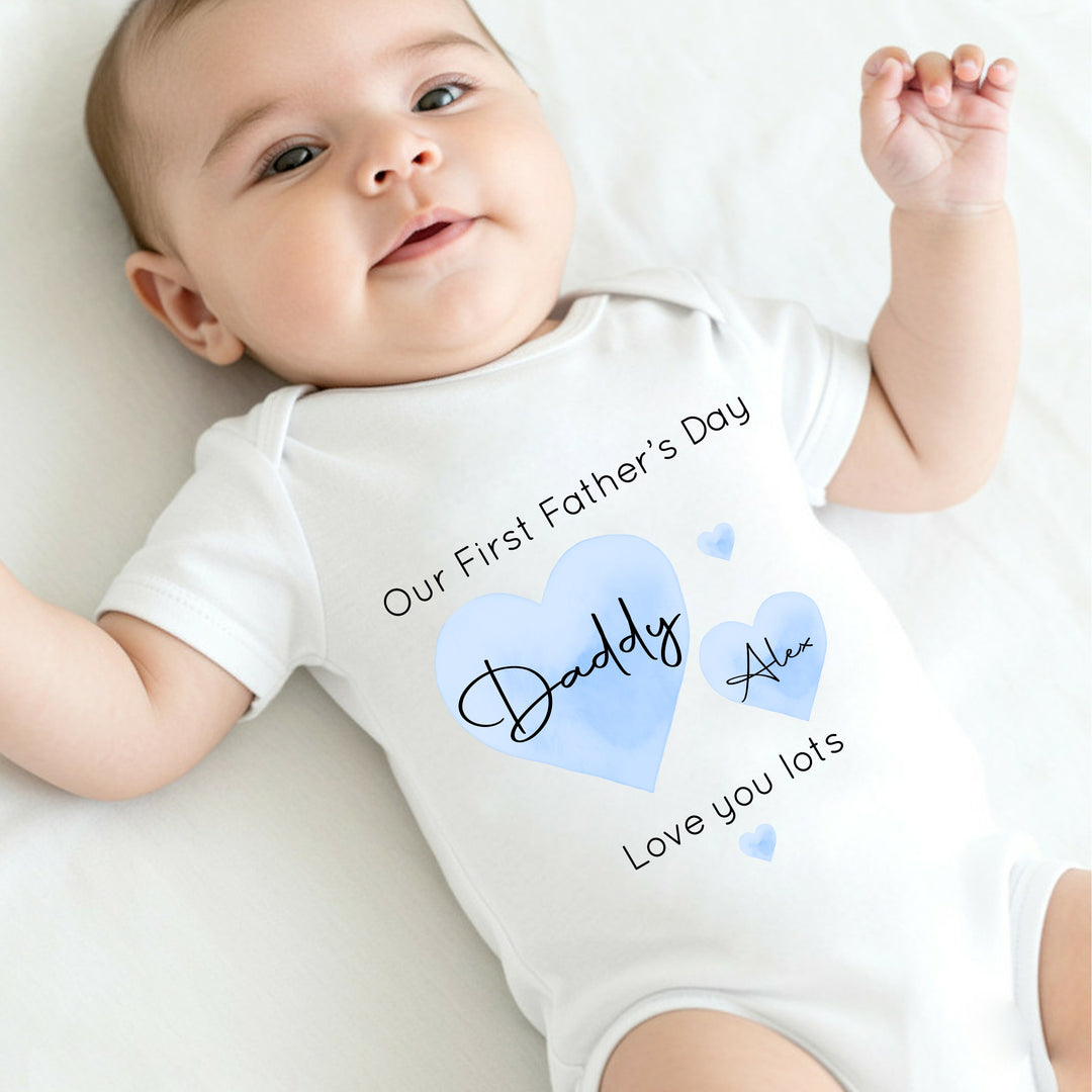 Personalised white Father's Day baby vest that says 'Our First Father's Day Daddy Alex Love you lots'. This design features 2 blue hearts