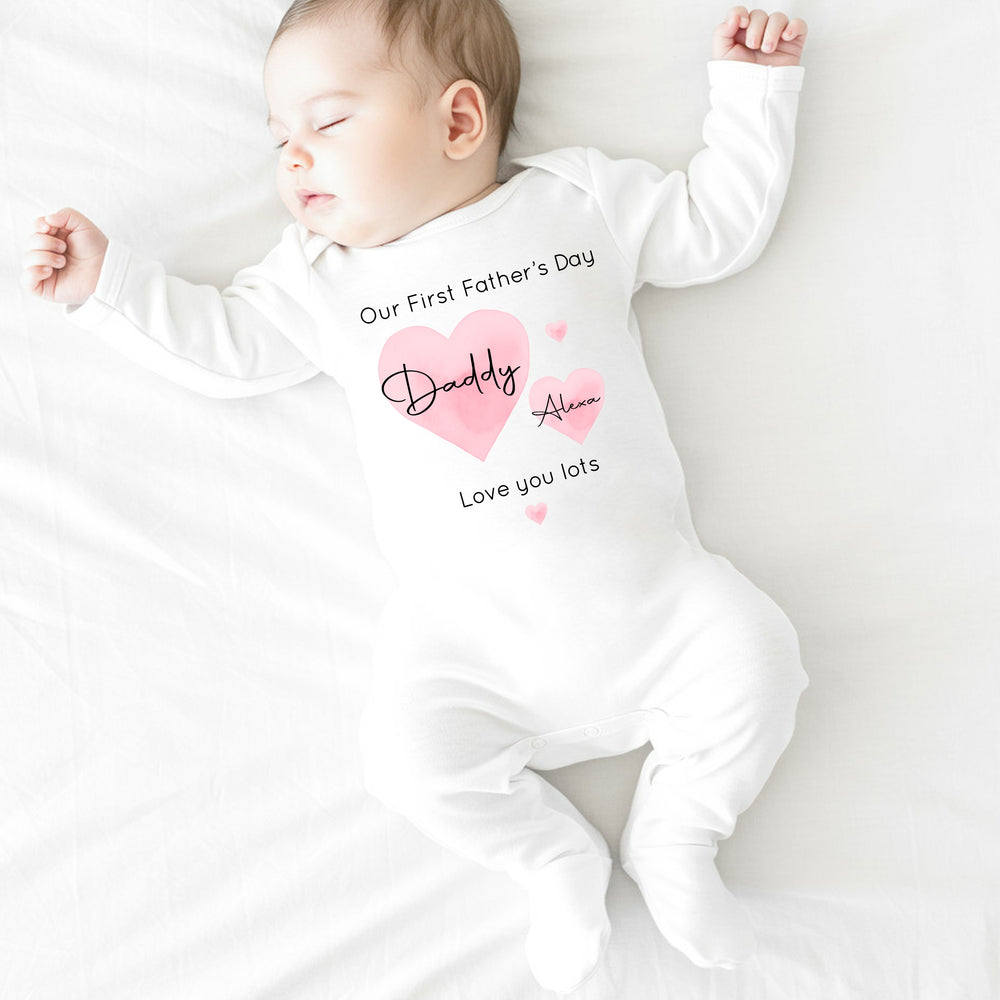 Personalised white Father's Day baby grow/sleepsuit that says 'Our First Father's Day Daddy Alexa Love you lots'. This design features 2 big pink hearts