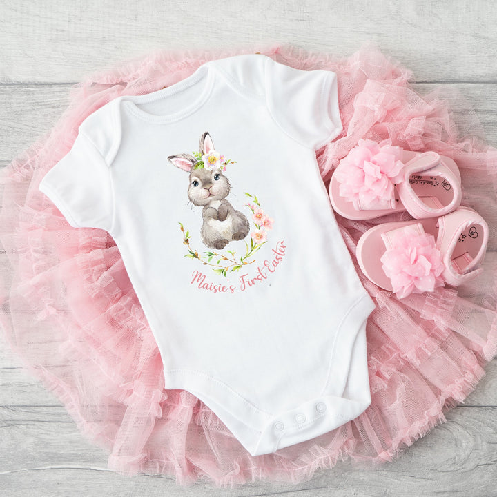 Personalised white Easter baby vest that says 'Maisie's First Easter'. This design features a grey rabbit in a pink floral wreath