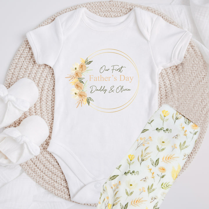 Personalised white Father's Day baby vest that says 'Our First Father's Day Daddy & Olivia'. This design features a peach leaf wreath