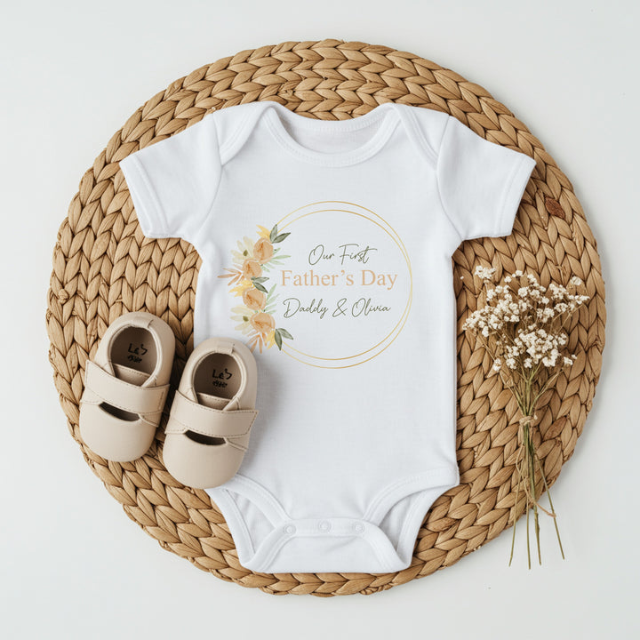 Personalised white Father's Day baby vest that says 'Our First Father's Day Daddy & Olivia'. This design features a peach leaf wreath