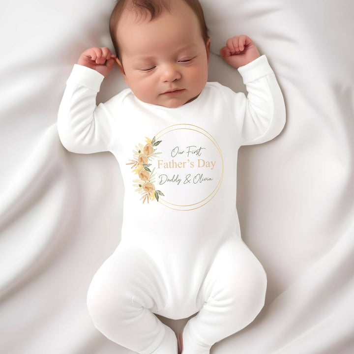 Personalised white Father's Day baby grow/sleepsuit that says 'Our First Father's Day Daddy & Olivia'. This design features a peach leaf wreath