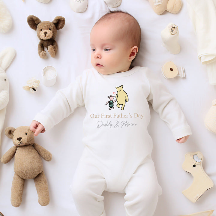 Personalised white Father's Day baby grow/sleepsuit that says 'Our First Father's Day Daddy & Finn'. This design features the Classic Winnie the Pooh and piglet holding hands