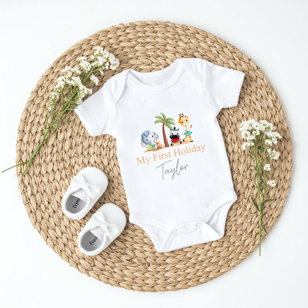 Personalised white baby vest that says 'My First Holiday Taylor'. This design features 3 cartoon characters standing around a palm tree