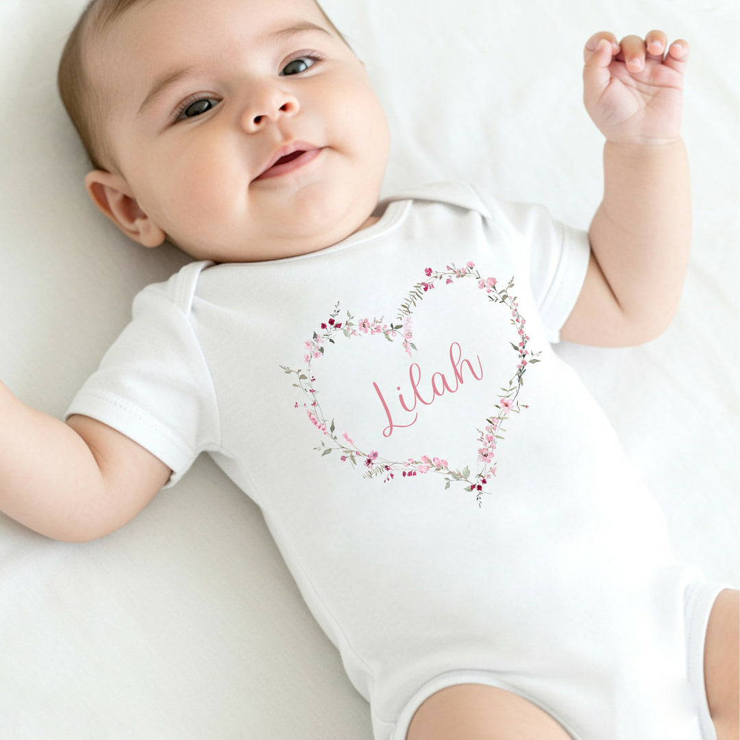 Personalised white baby vest that says 'Lilah'. This design features a pink floral heart with a name in the middle