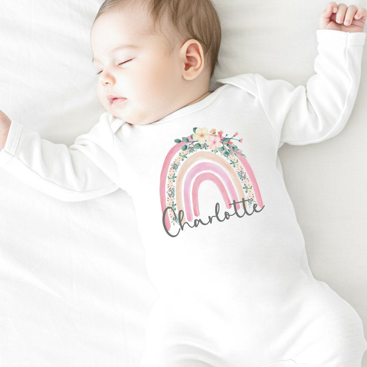 a personalised white baby grow that says 'Charlotte'. This design features a pink floral rainbow