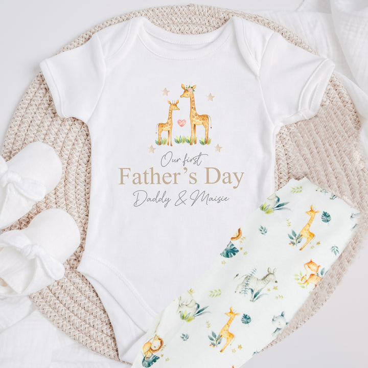 Personalised white Father's Day baby grow/sleepsuit that says 'Our First Father's Day Daddy & Maisie'. This design features 2 giraffes