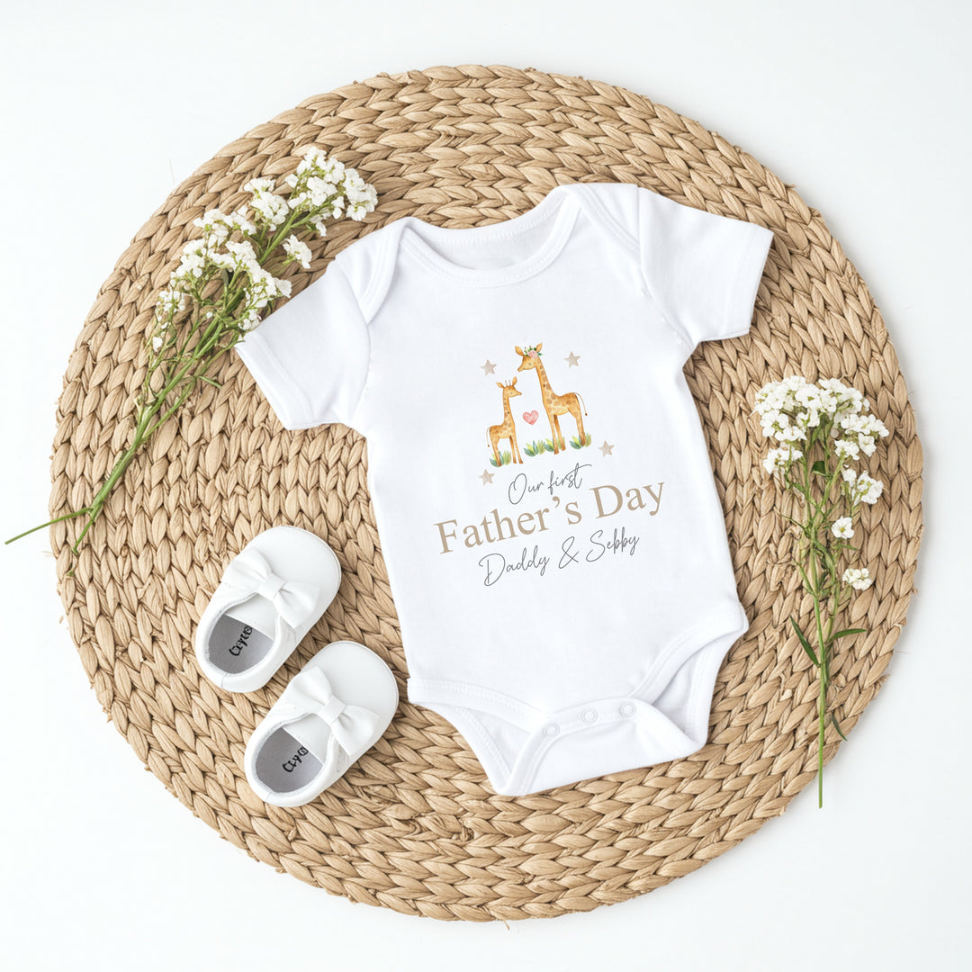 Personalised white Father's Day baby vest that says 'Our First Father's Day Daddy & Sebby'. This design features 2 giraffes