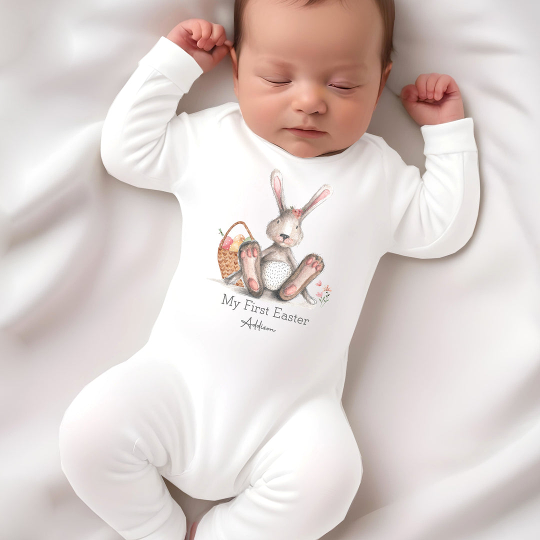 Personalised white Easter baby grow/sleepsuit that says 'My First Easter Addison'. This design features a grey bunny with pink details sitting next to an Easter basket