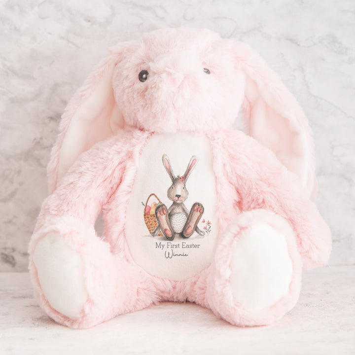 Personalised pink bunny Easter teddy that says 'My First Easter Winnie'. This design features a grey bunny with a pink bow sitting next to a basket full of Easter eggs