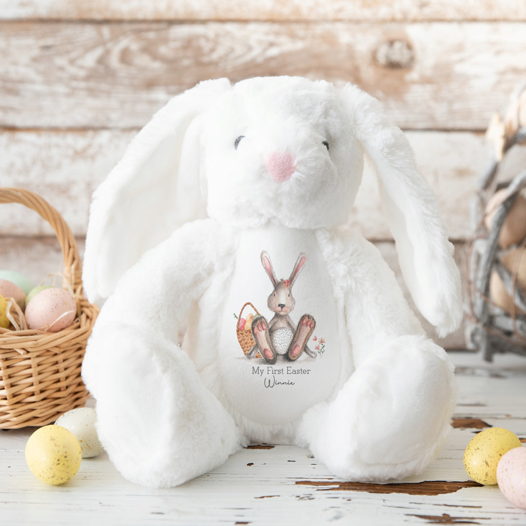 Personalised white bunny Easter teddy that says 'My First Easter Winnie'. This design features a grey bunny with a pink bow sitting next to a basket full of Easter eggs